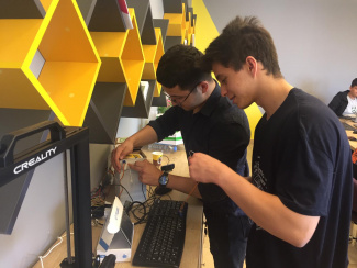 Two boys connecting cables to recycling boxes with motorised lids