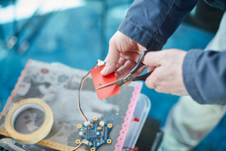 A person cutting through a piece of paper with a sensor strip. The paper with the sensor is connected to a Calliope microcontroller.